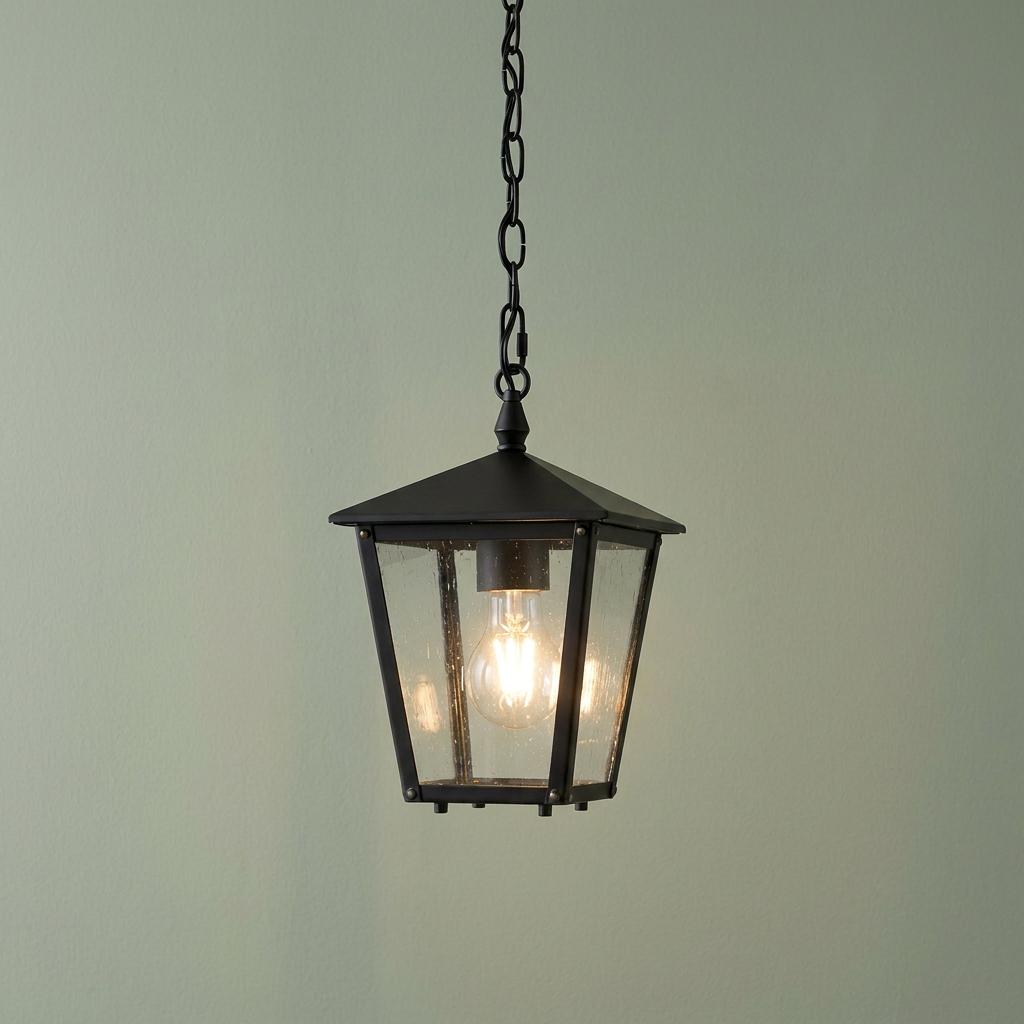 Hinkley Huntersfield small black outdoor chain lantern with seeded glass panels hanging against a light green wall.
