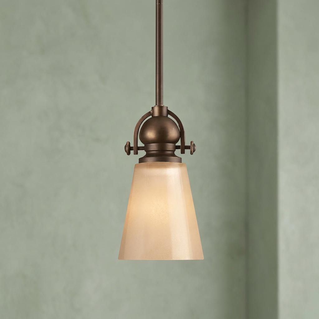 Hinkley Mayflower bronze small pendant light with an amber glass shade against a light green wall.
