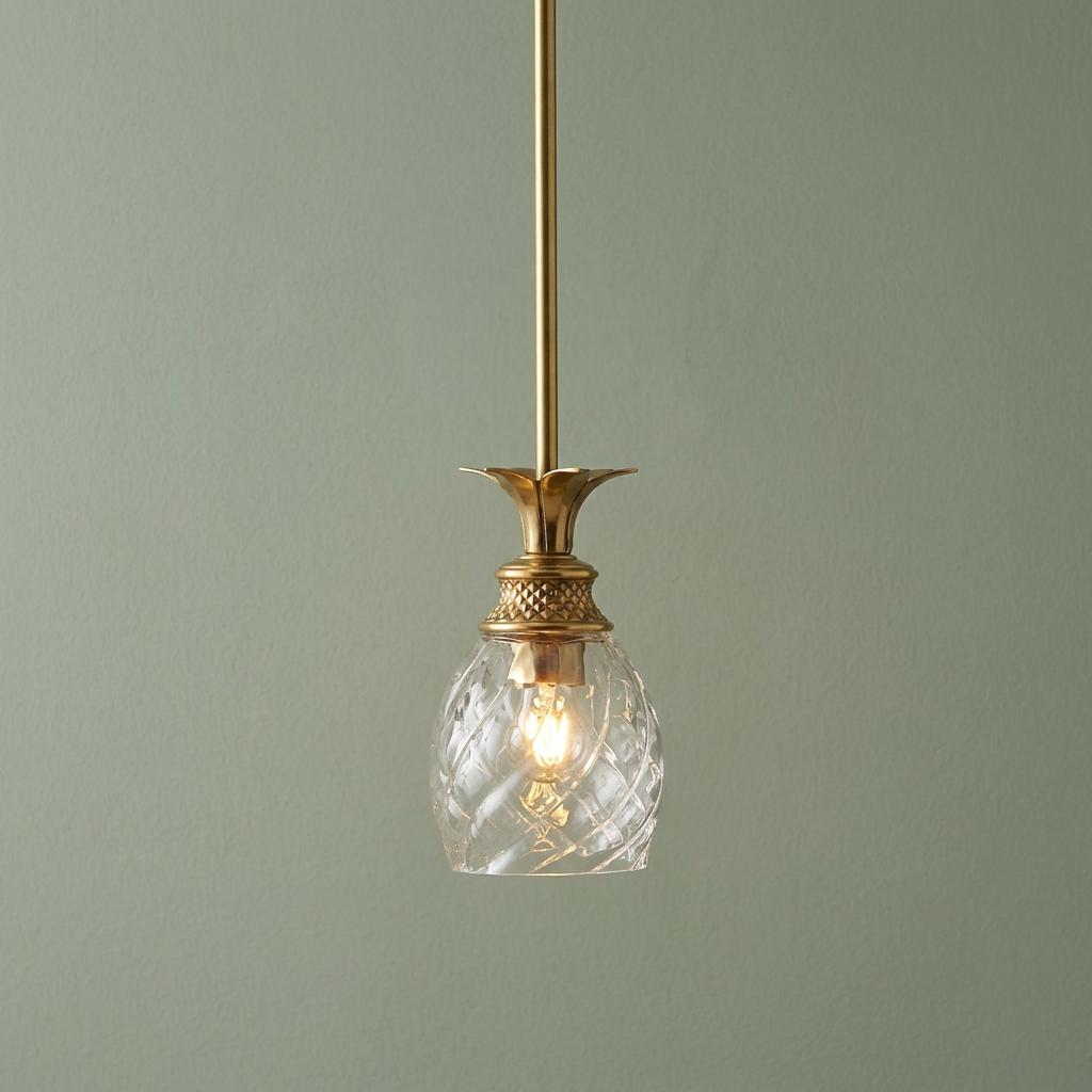 Hinkley Plantation brass pendant with a pineapple-style optic glass shade illuminated against a soft green wall.