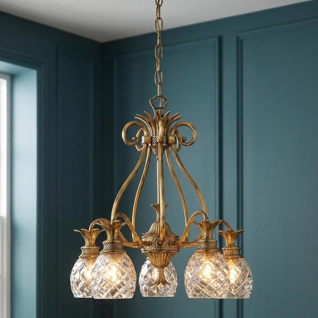 Hinkley Plantation 5-light brass chandelier with ornate pineapple-shaped glass shades against a teal paneled wall.