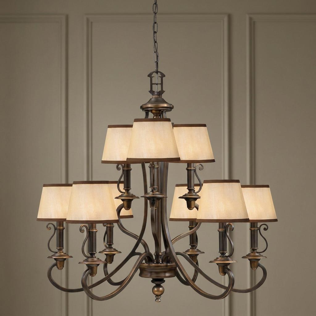 Old bronze 9-light chandelier with two tiers of cream fabric shades and scrolled arms against a paneled wall.