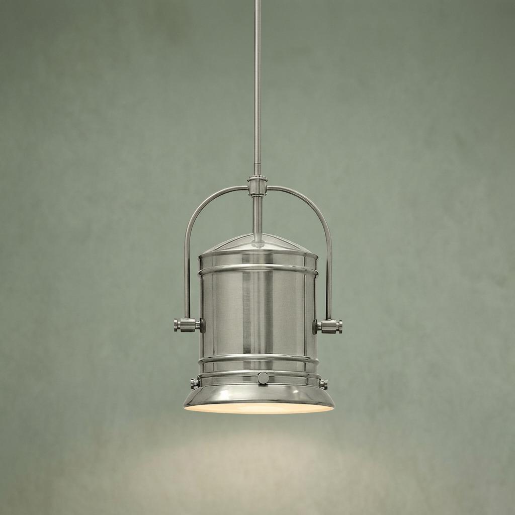 Industrial brushed nickel ceiling pendant with a cylindrical shade and metal yoke against a green wall.