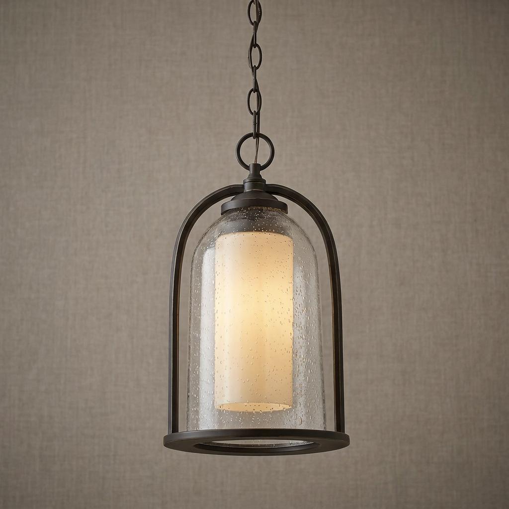 An oil rubbed bronze outdoor pendant light with a clear seeded glass cloche and white interior cylinder.