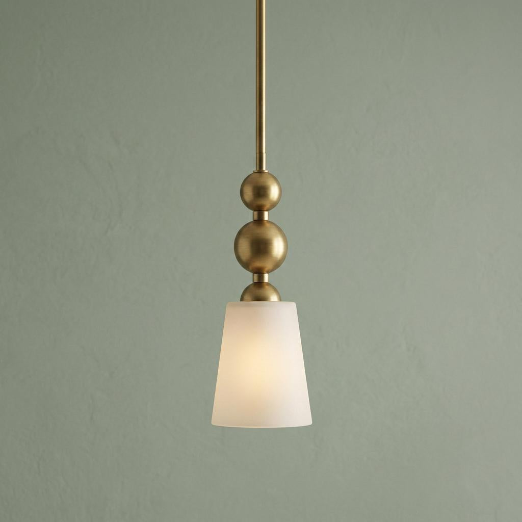 Vintage brass mini pendant with stacked sphere details and a frosted glass shade glowing against a green wall.