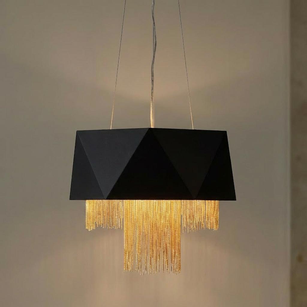 Black geometric pendant light with tiered gold chains hanging below, glowing against a neutral wall.