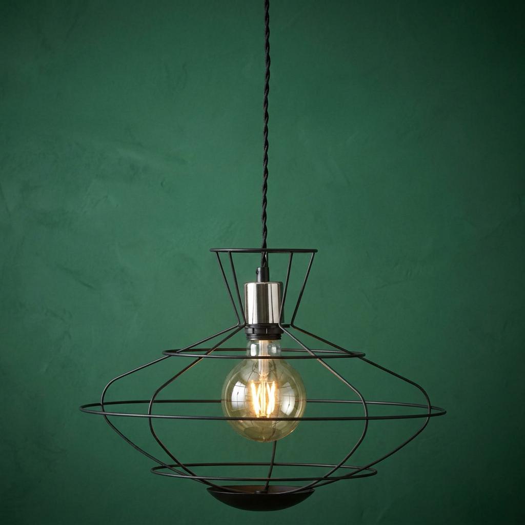 Industrial black cage pendant light with a chrome bulb holder and glowing Edison bulb against a dark green wall.