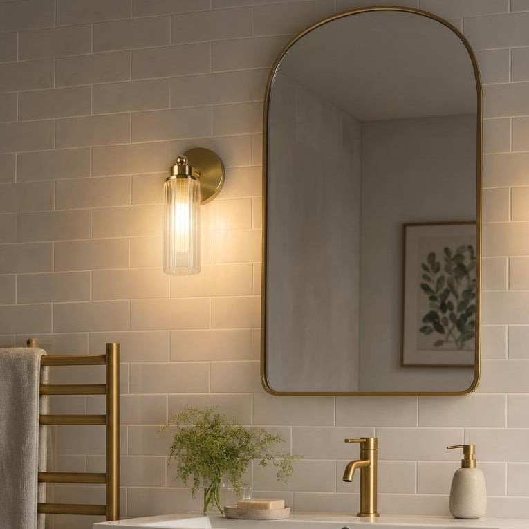 A pair of brass fluted glass wall sconces flanking an arched mirror in a modern tiled bathroom.