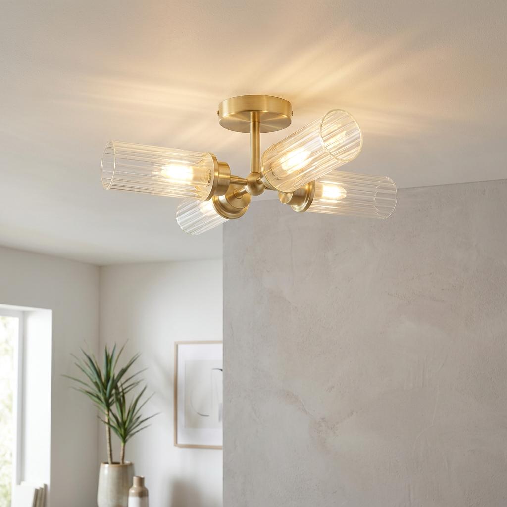 Satin brass ceiling light with four ribbed glass cylinders mounted on a white ceiling in a contemporary interior.