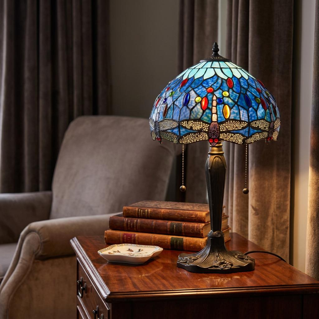 Blue dragonfly Tiffany table lamp with an ornate shade, sitting on a wooden side table next to vintage books.