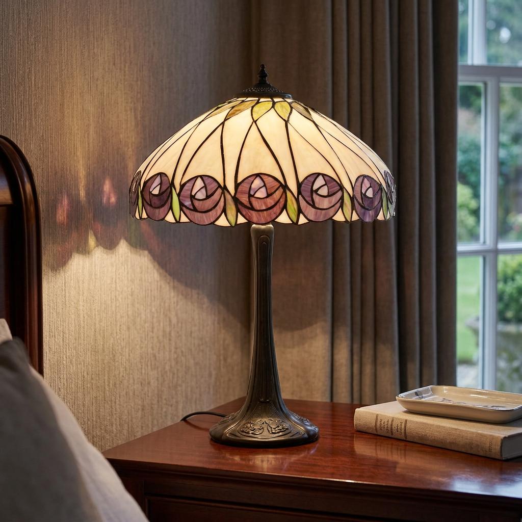 A Tiffany table lamp with a purple rose patterned glass shade sits illuminated on a wooden bedside table.