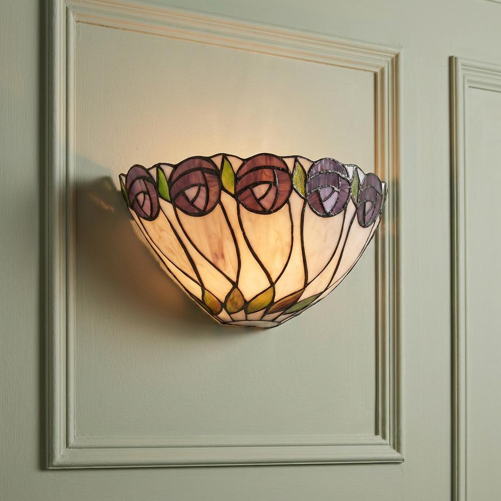 Leaded Tiffany wall light with purple rose motif and warm glow on a green paneled wall.