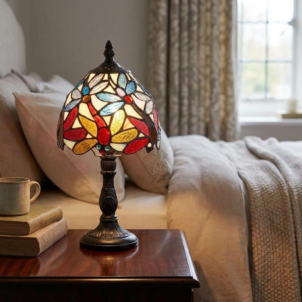 Lorette Tiffany bedside lamp with colorful stained glass shade on a dark wooden nightstand in a soft-lit bedroom.