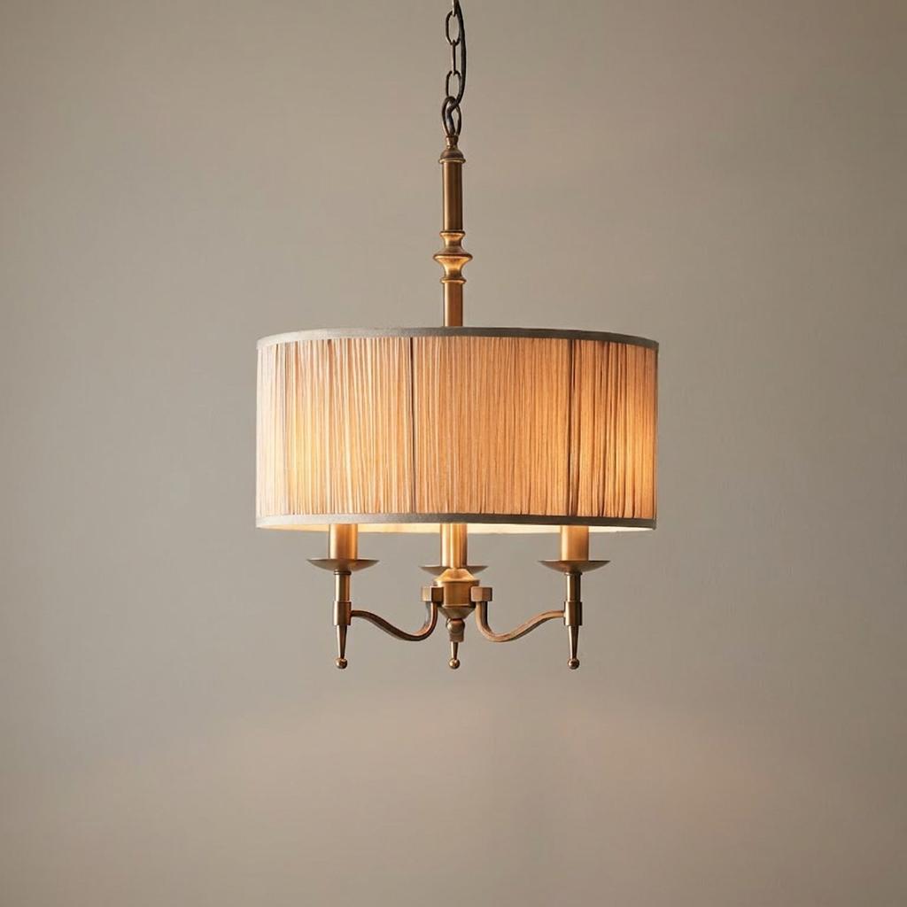 Antique brass 3-light pendant featuring a beige pleated drum shade hanging against a neutral background.