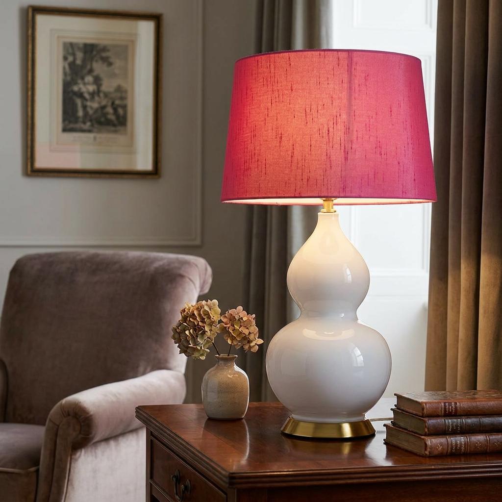 Isla White Ceramic Table Light with a cranberry shade on a wooden side table in a cozy living room.