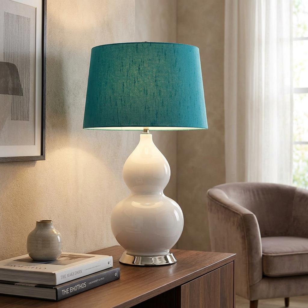 White ceramic gourd table lamp with a teal textured shade on a wooden sideboard in a living room.