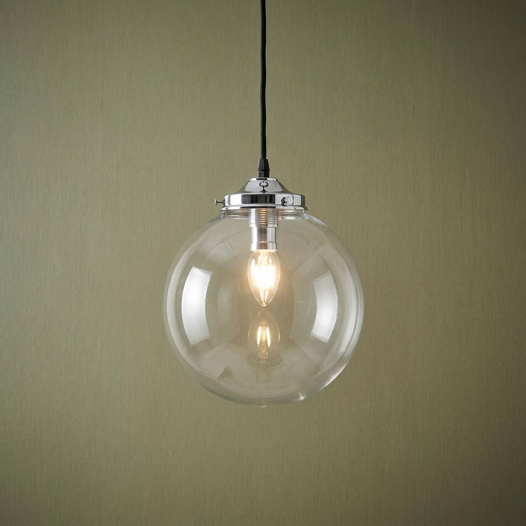 Extra large clear glass globe pendant light with a chrome fixture and lit bulb on a textured green background.