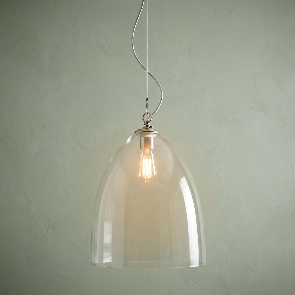 Large clear glass dome pendant light with an exposed filament bulb against a pale green textured wall.