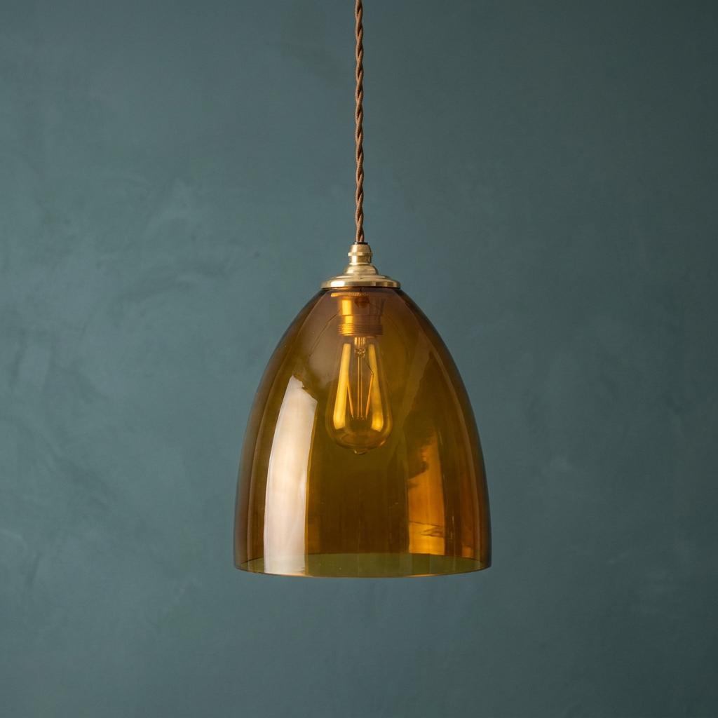Whisky-toned dome glass pendant light with brass hardware and twisted cable against a blue-green wall.