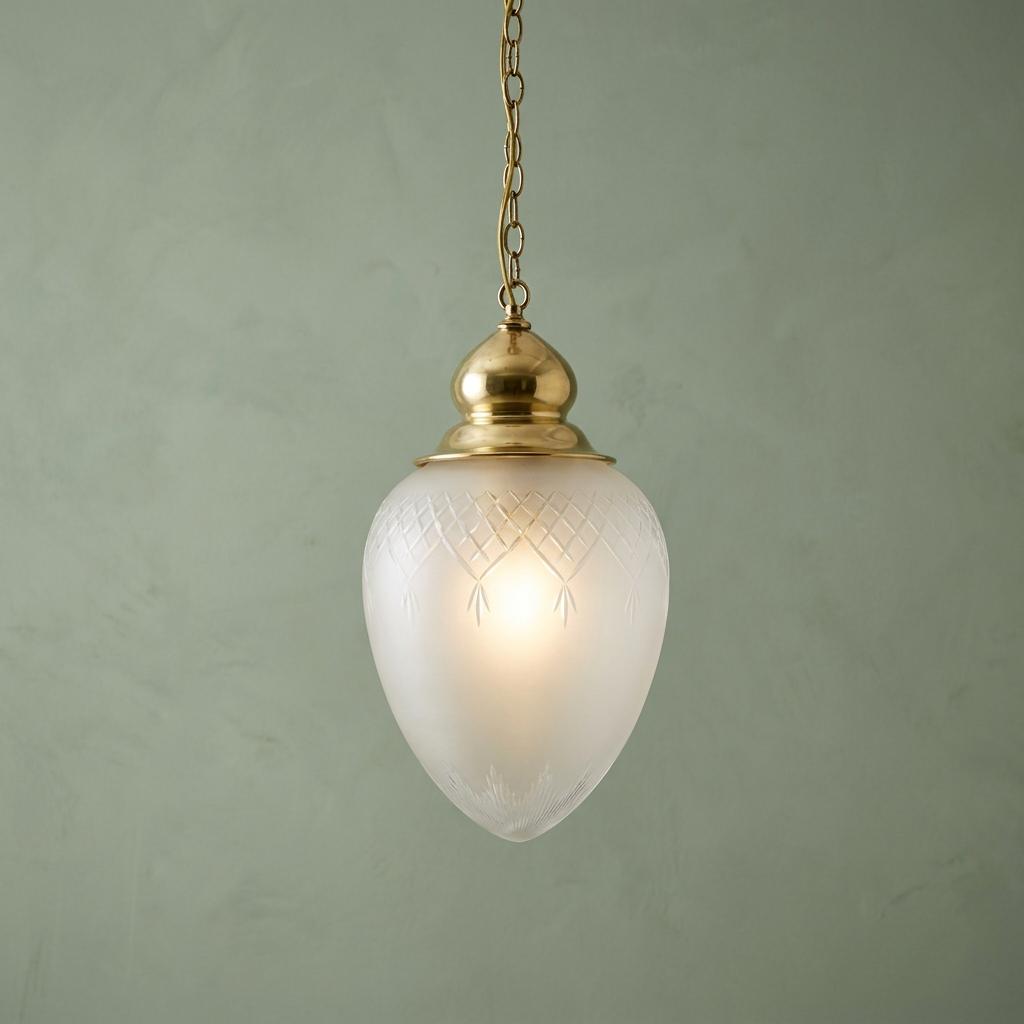 Glowing frosted glass pineapple pendant light with brass fittings against a textured green wall.