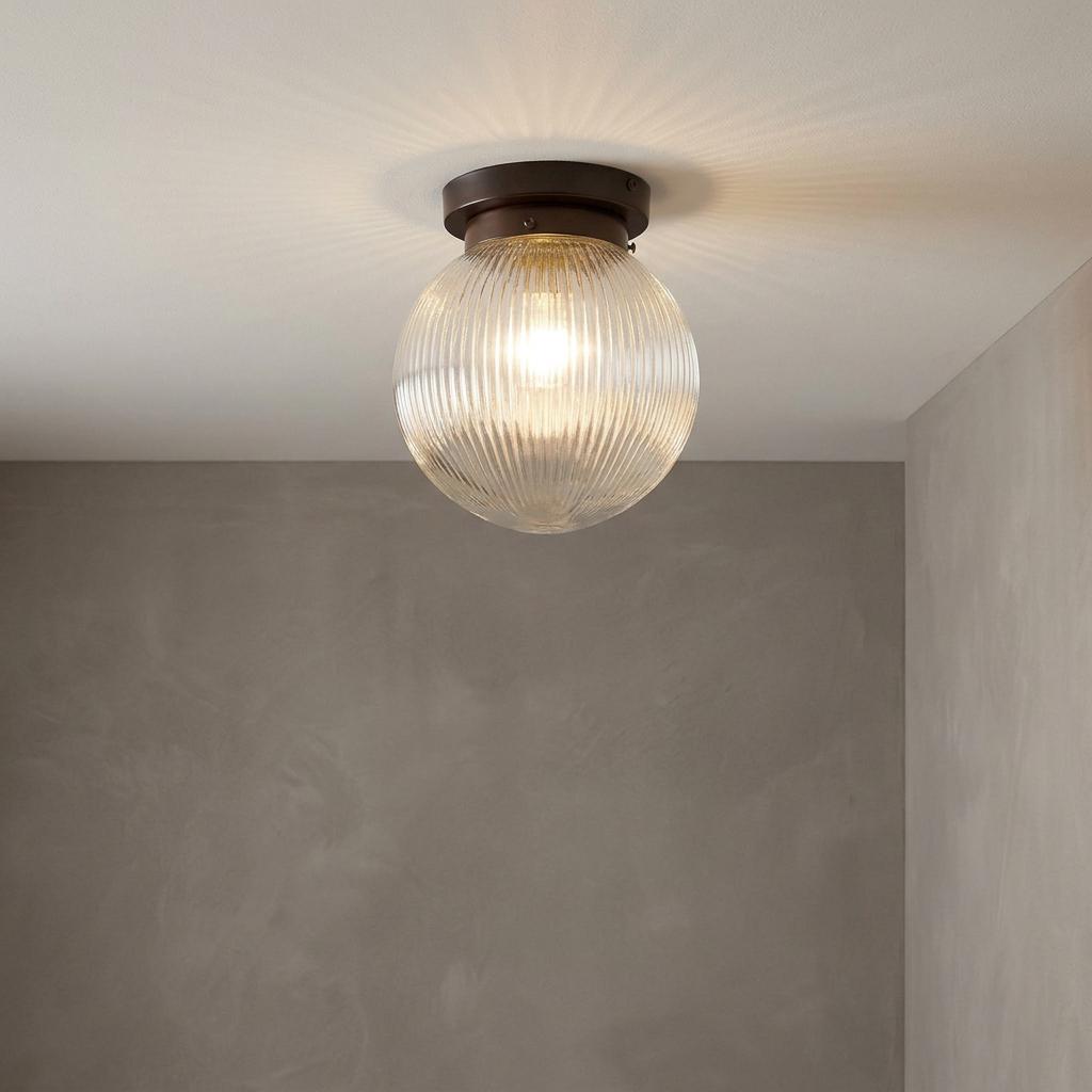 Prismatic glass globe flush mount ceiling light with a bronze base, illuminated against a grey textured wall.