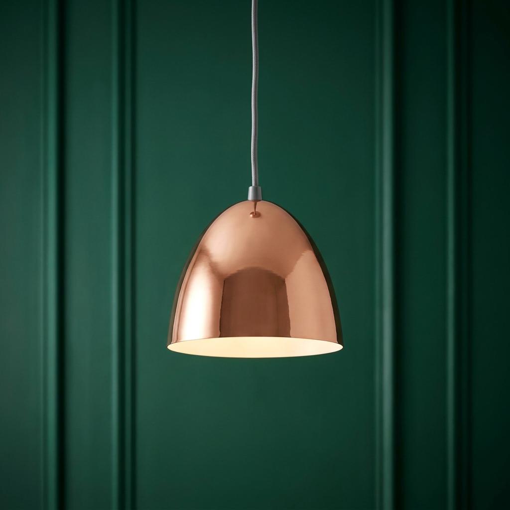 Polished copper dome pendant light with warm internal glow against a dark green wood-paneled wall.