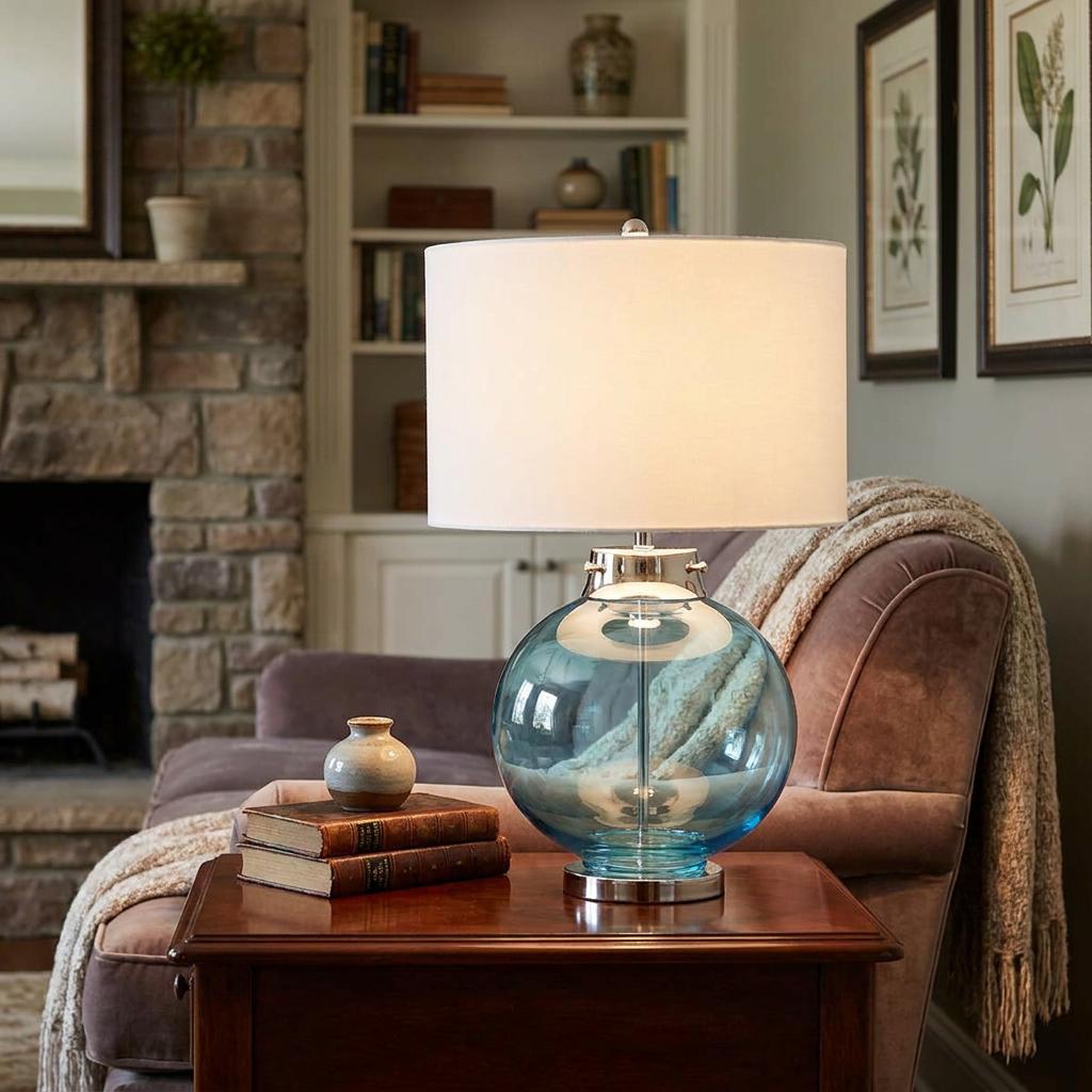 Kara Blue Glass Table Lamp with white drum shade on a wooden end table in a warm living room.