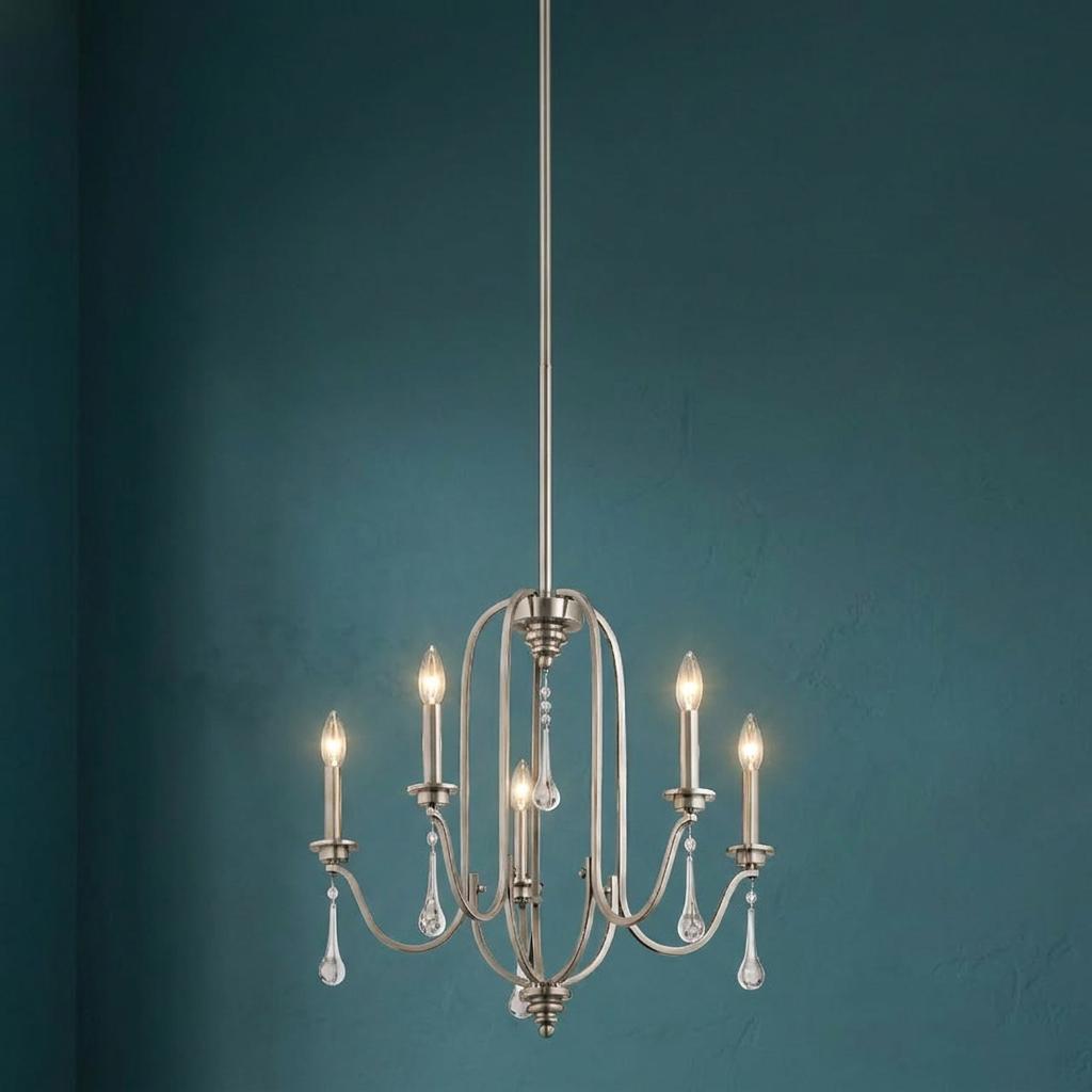 Five-light pewter chandelier with candle bulbs and crystal droplets against a textured teal wall.