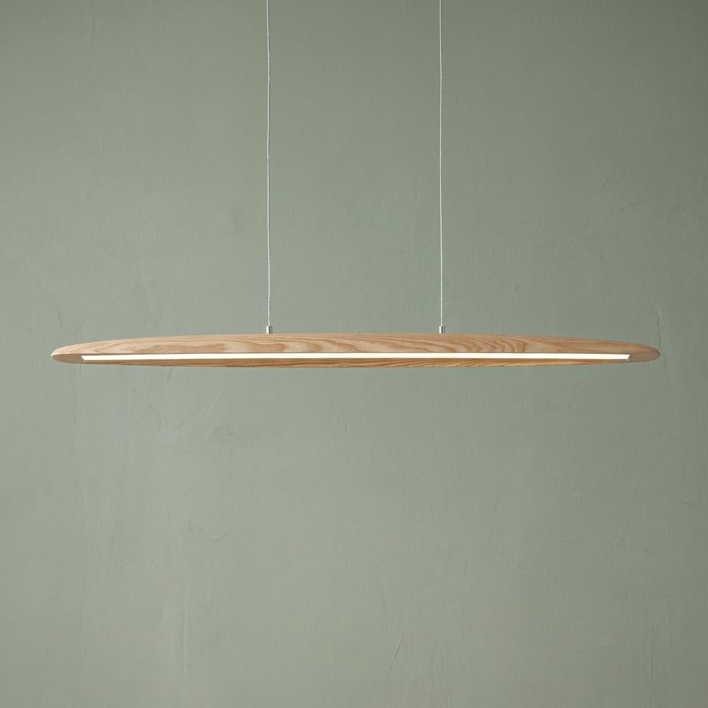 A slim natural wood linear pendant light with an integrated LED strip hanging against a sage green textured wall.