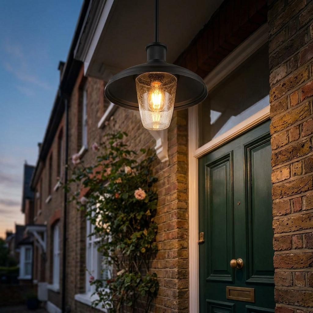 Black outdoor pendant light with seeded glass illuminates a brick house entrance with a green door.
