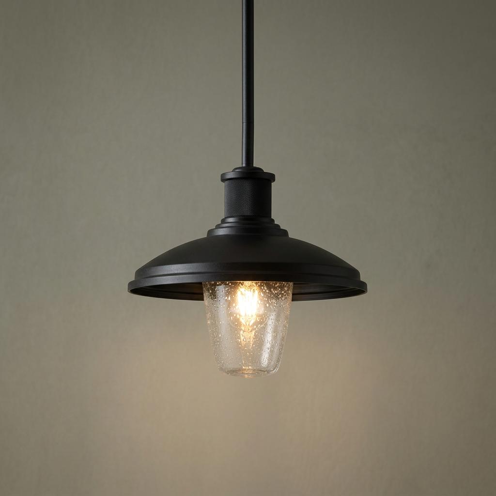 Kichler Allenbury black outdoor pendant light with a seeded glass shade and glowing bulb against a neutral wall.