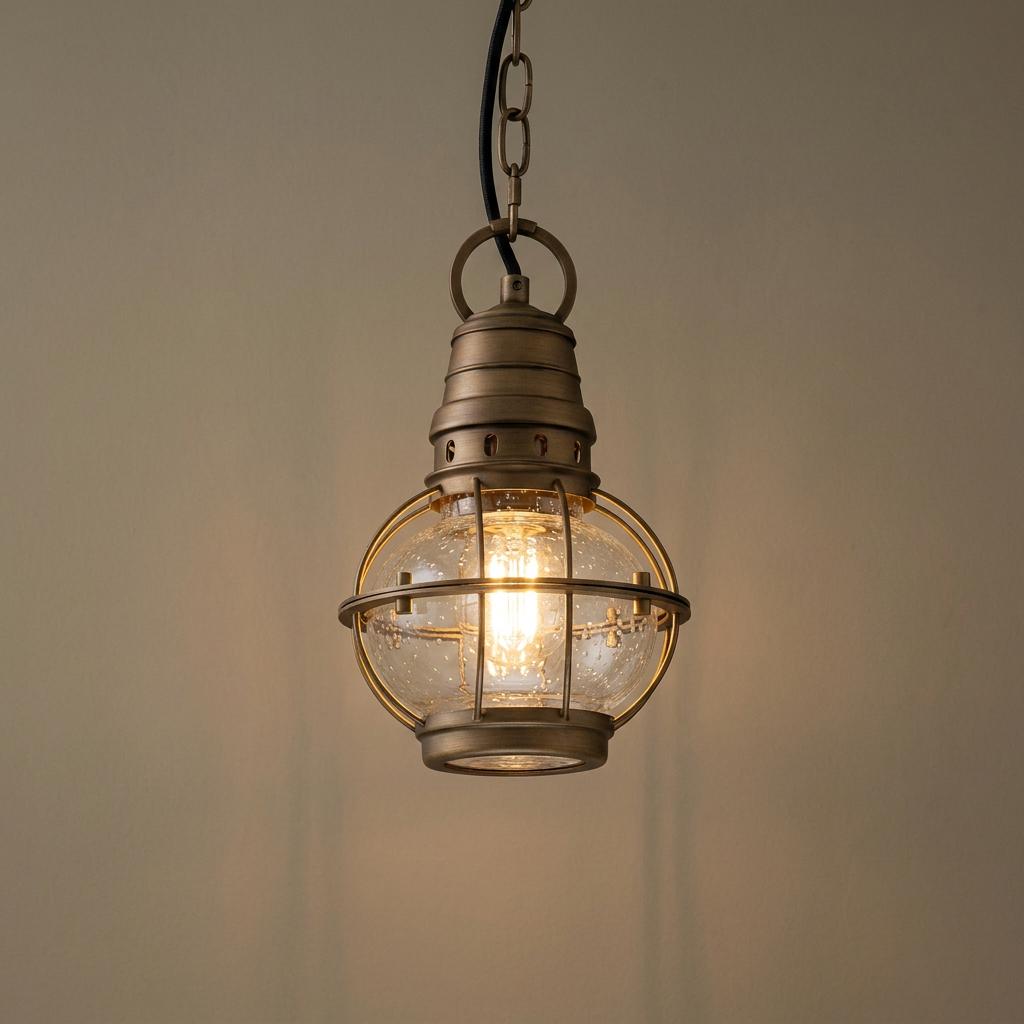 Kichler Bridgepoint brass outdoor chain lantern with a seeded glass globe and nautical cage, illuminated.