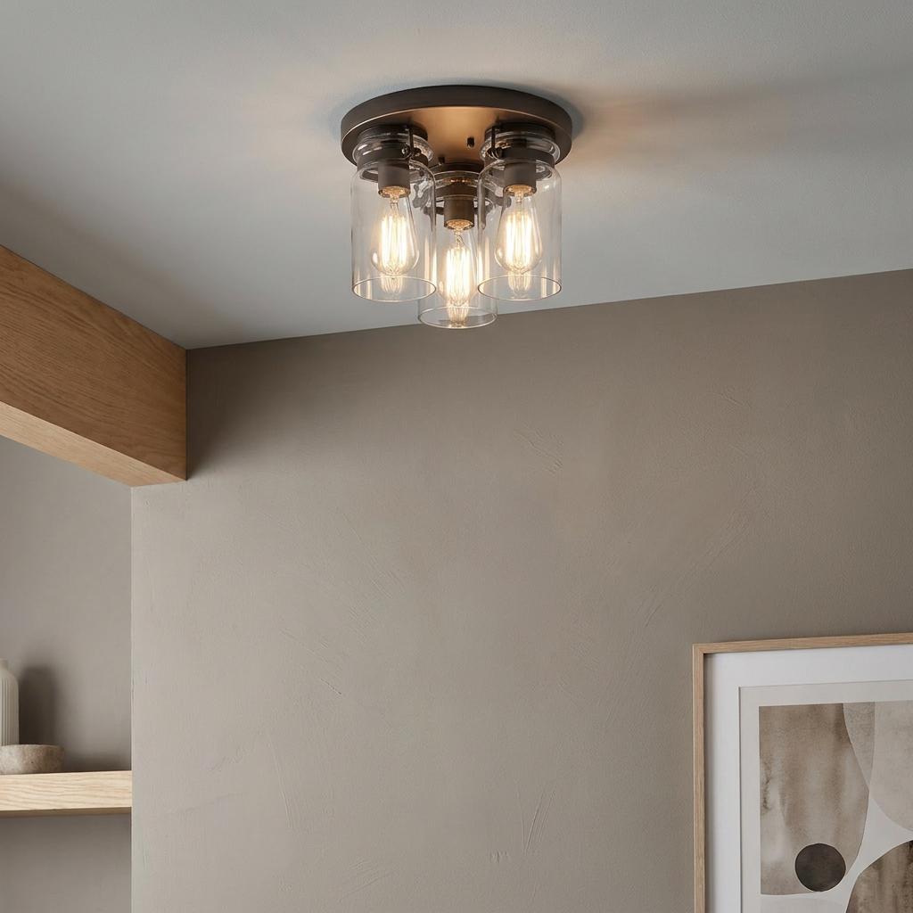 Three-light bronze flush mount ceiling fixture with clear glass jar shades and warm glowing Edison bulbs.