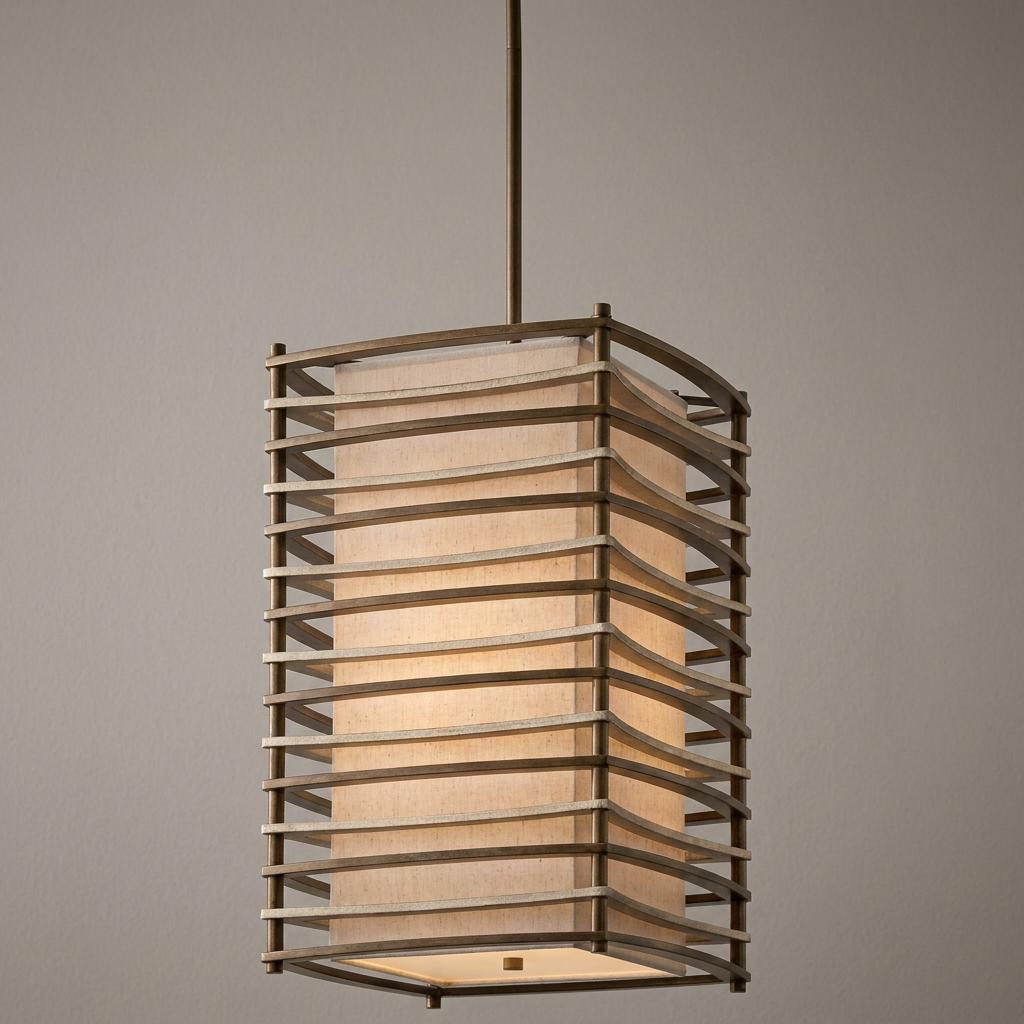 Large bronze pendant light with a fabric shade encased in a curved horizontal slat metal frame.