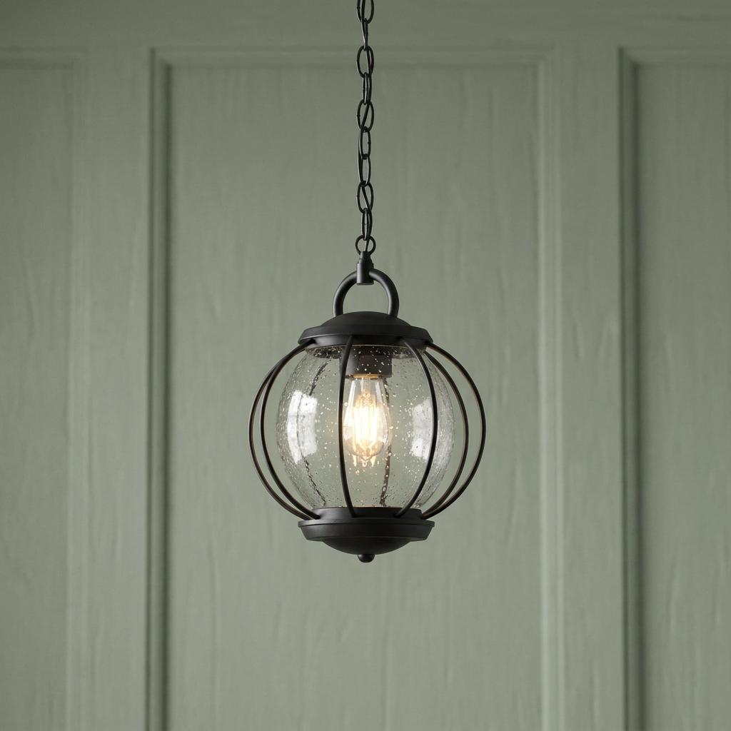 Kichler Vandalia black outdoor pendant with seeded glass and metal cage hangs against a pale green paneled wall.