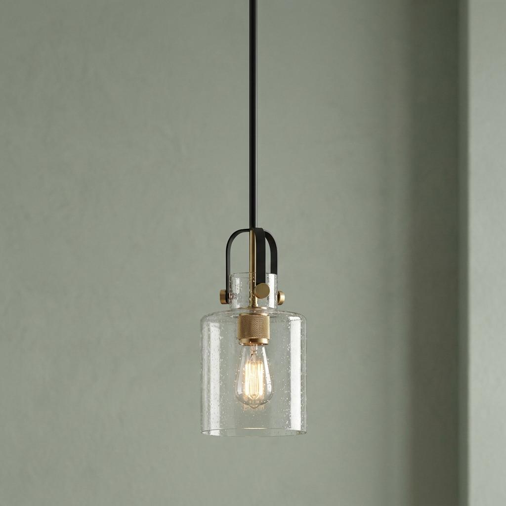 Modern pendant light with clear seeded glass cylindrical shade and brass socket against a soft green wall.