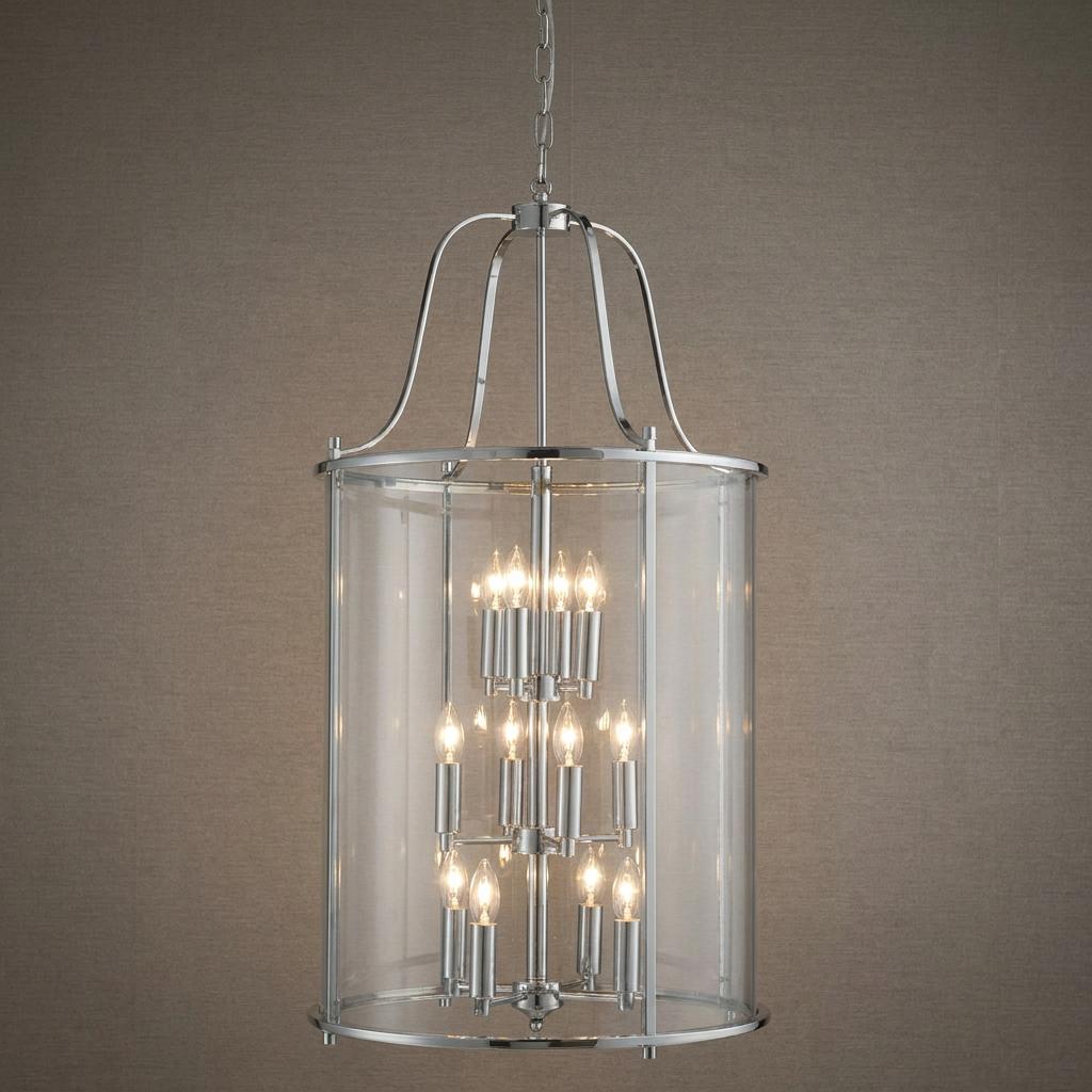 Large cylindrical chrome and clear glass lantern with twelve illuminated candle-style bulbs against a neutral wall.