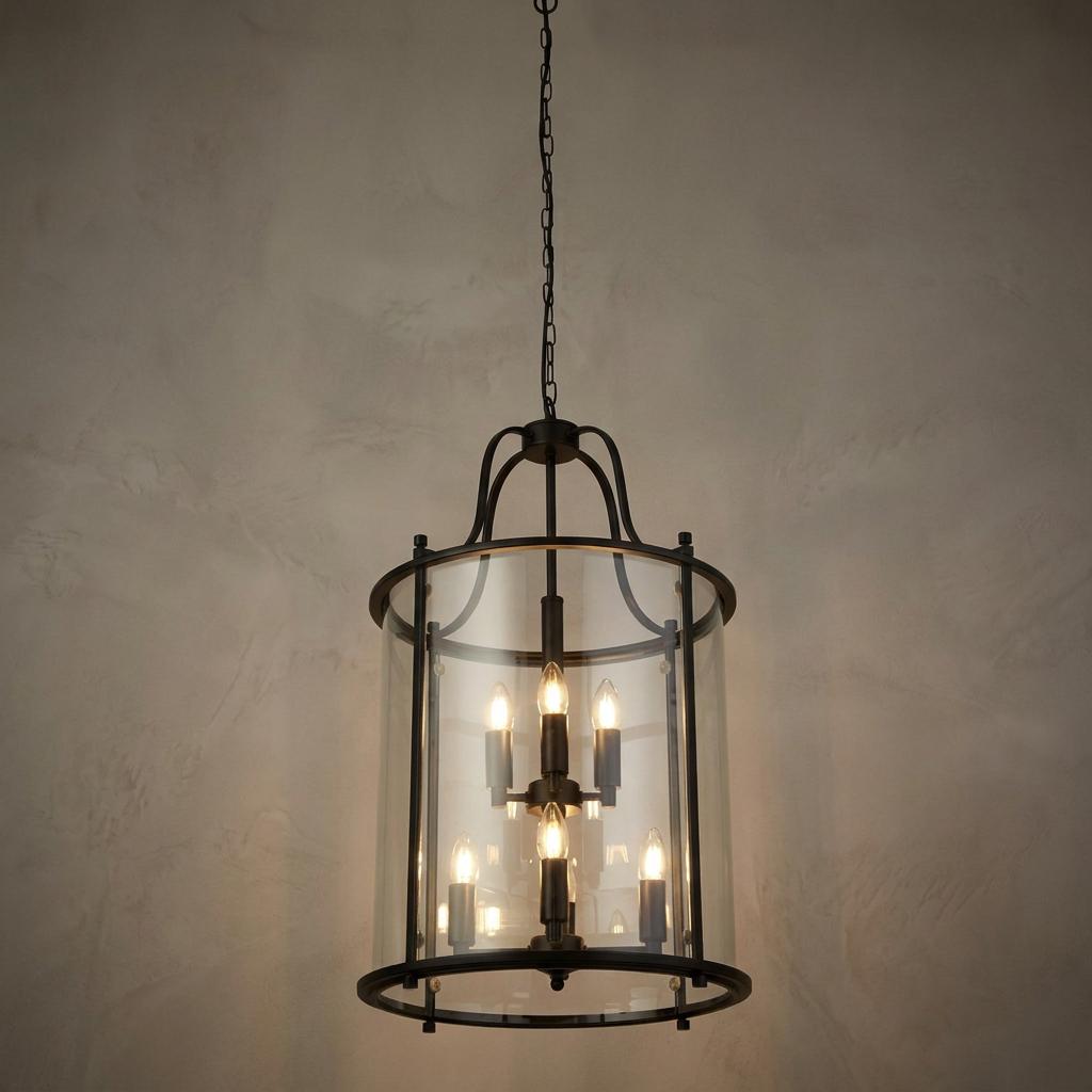 Eight-light black metal lantern with cylindrical clear glass suspended by a chain against a neutral wall.