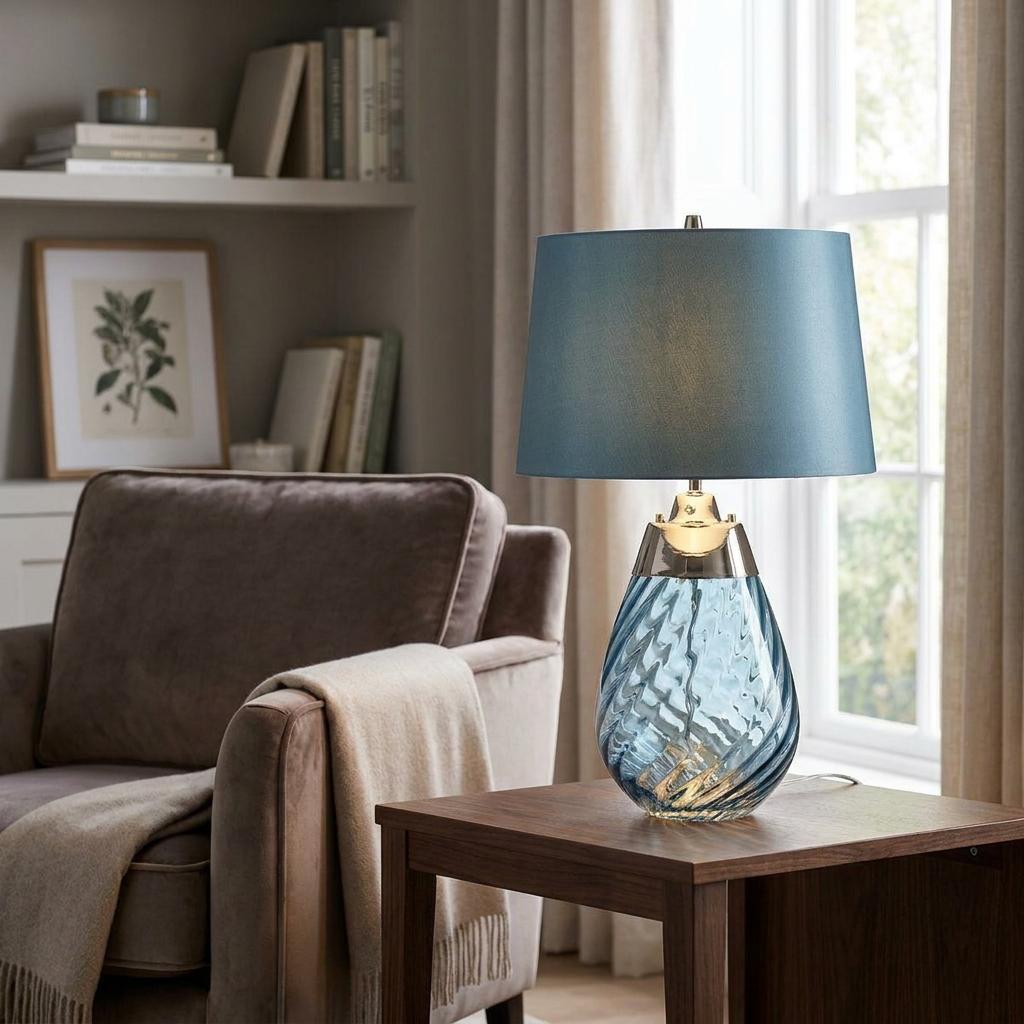 Blue swirl glass table lamp with a matching shade glowing on a wooden side table in a living room.