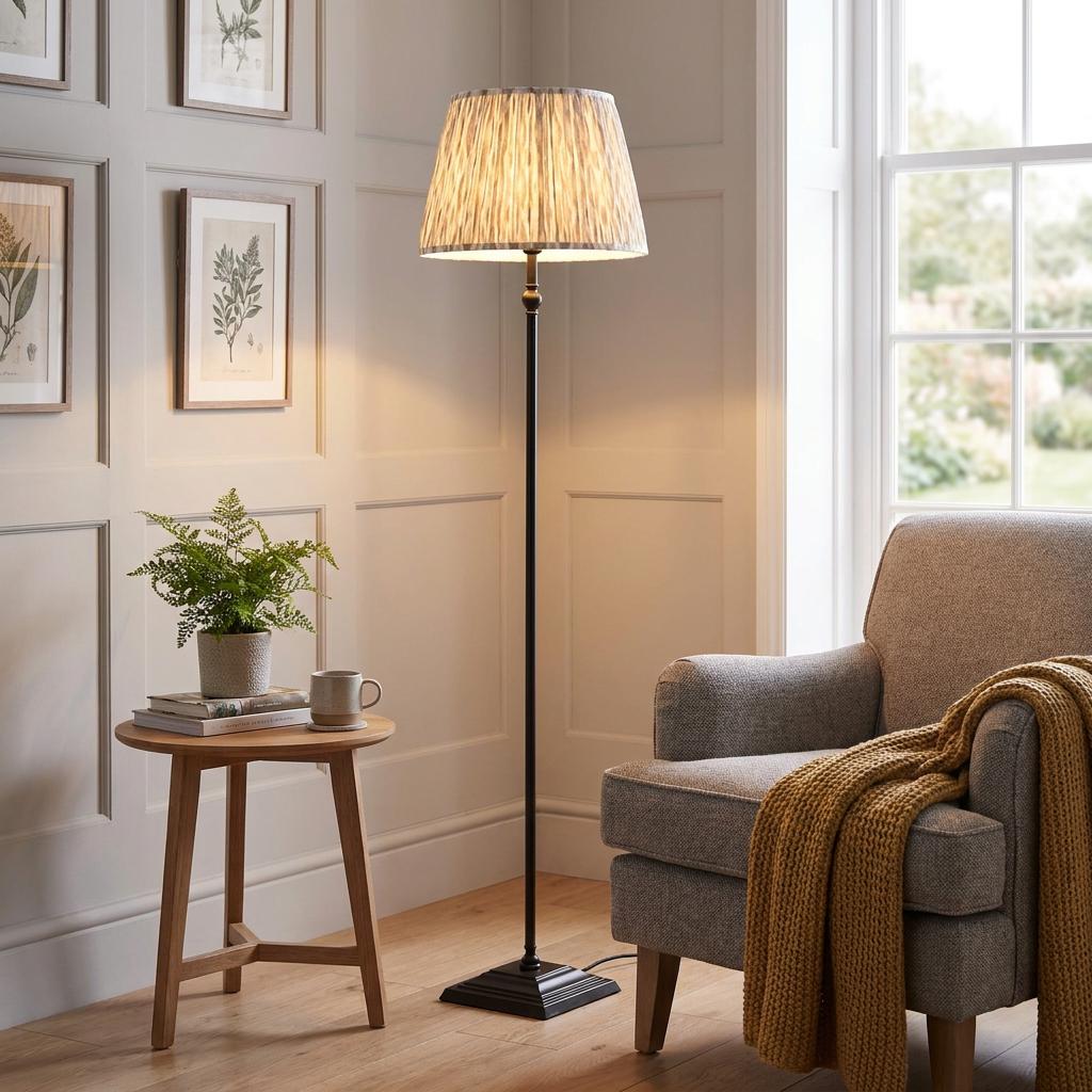 A black floor lamp with a neutral ikat shade stands between a grey armchair and a wooden side table in a living room.