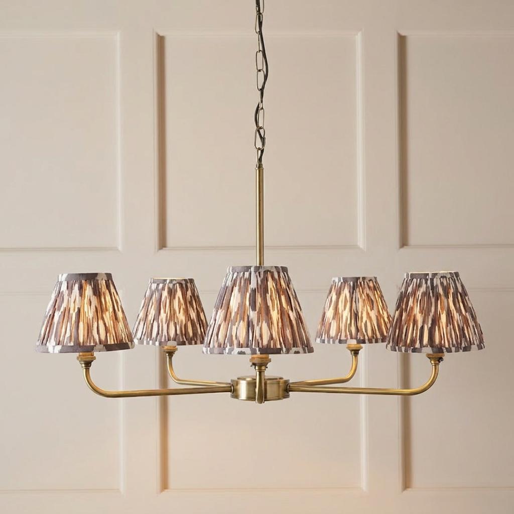 Lille brass 5-light pendant with grey Ikat pleated shades hanging against a cream paneled wall.