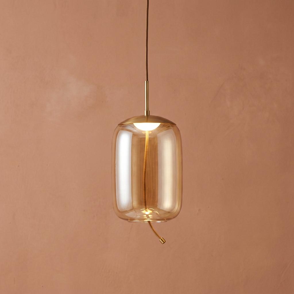 Lisbon 1 light LED pendant with a satin brass finish and amber glass shade against a terracotta wall.
