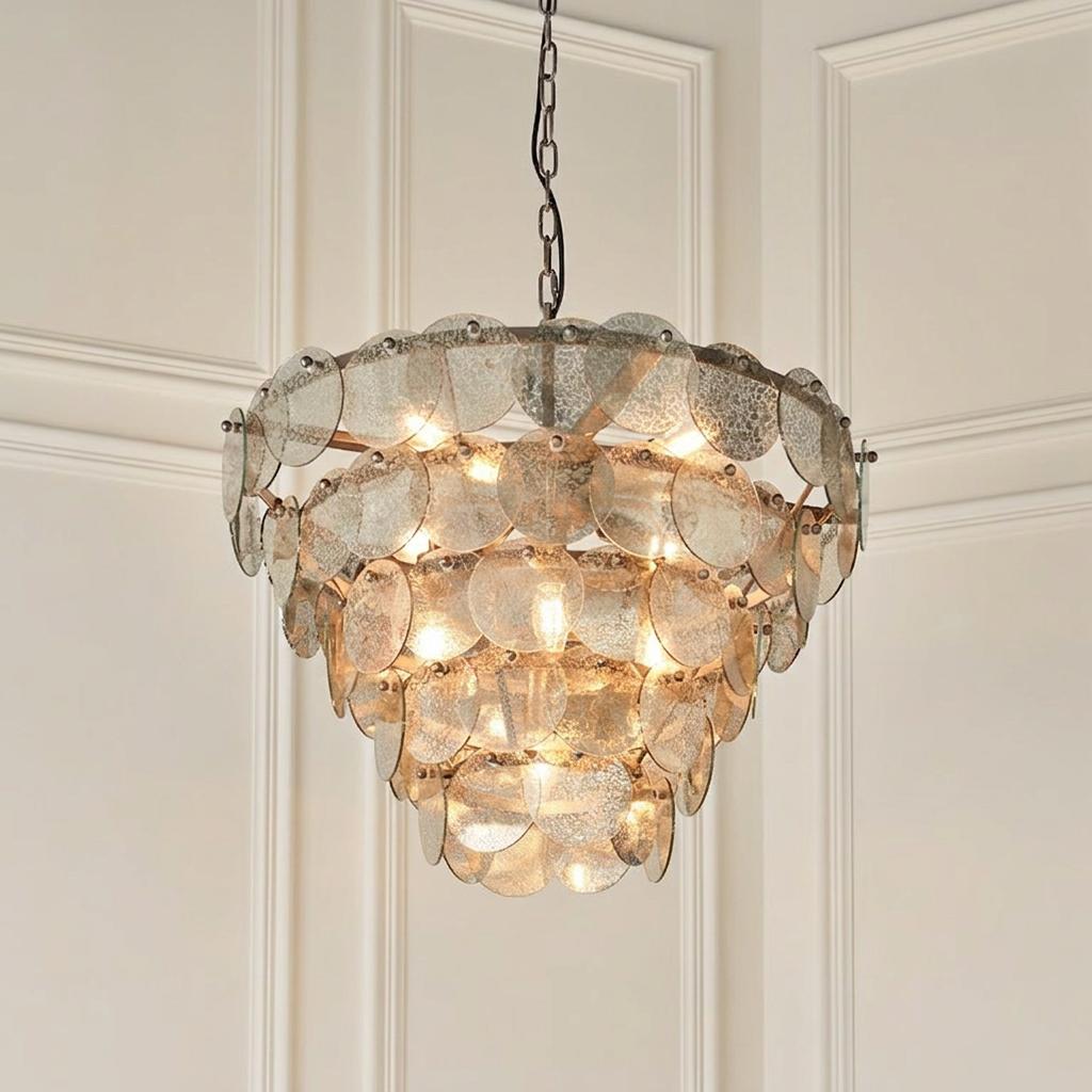 Tiered silver pendant light with mercury glass discs, illuminated against a white paneled wall.