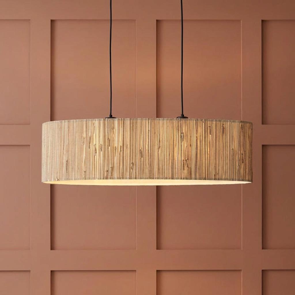 Linear pendant light with natural seagrass shade suspended against a terracotta paneled wall.