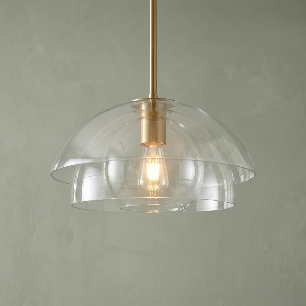 Lotus-style pendant light featuring tiered clear glass domes and brass hardware against a muted green wall.