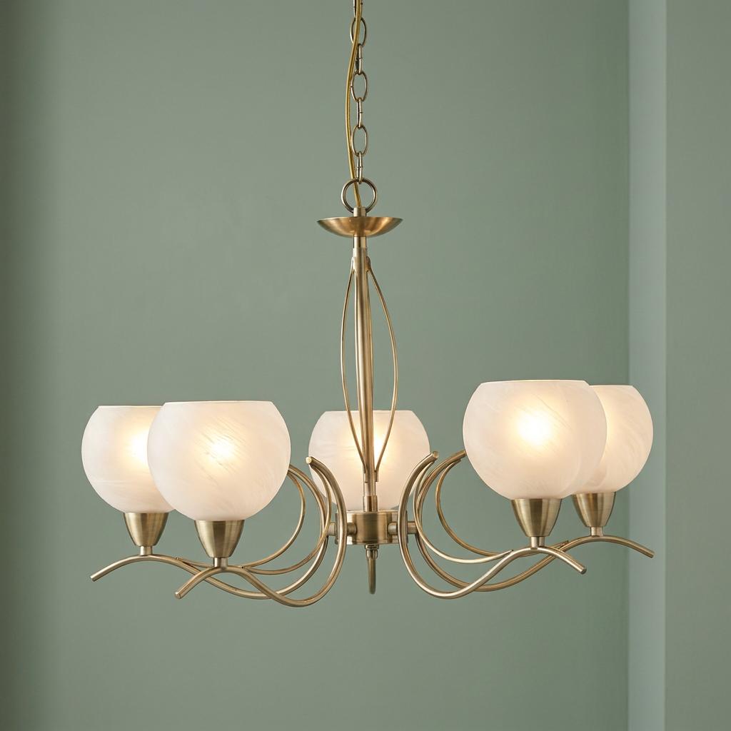 Five-light antique brass chandelier with curved arms and frosted glass bowl shades against a light green wall.