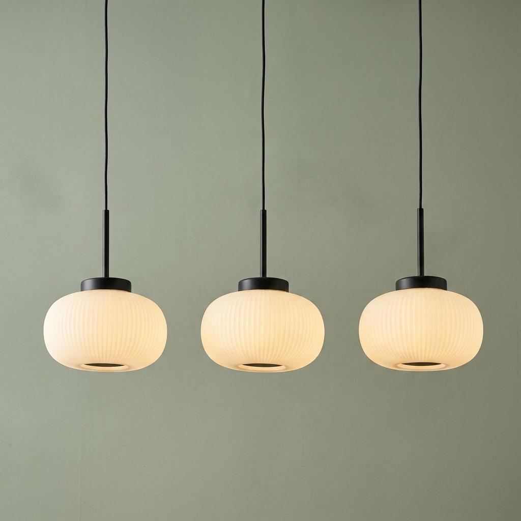 Three Lumina pendant lights with frosted ribbed glass globes and black fixtures against a sage green wall.