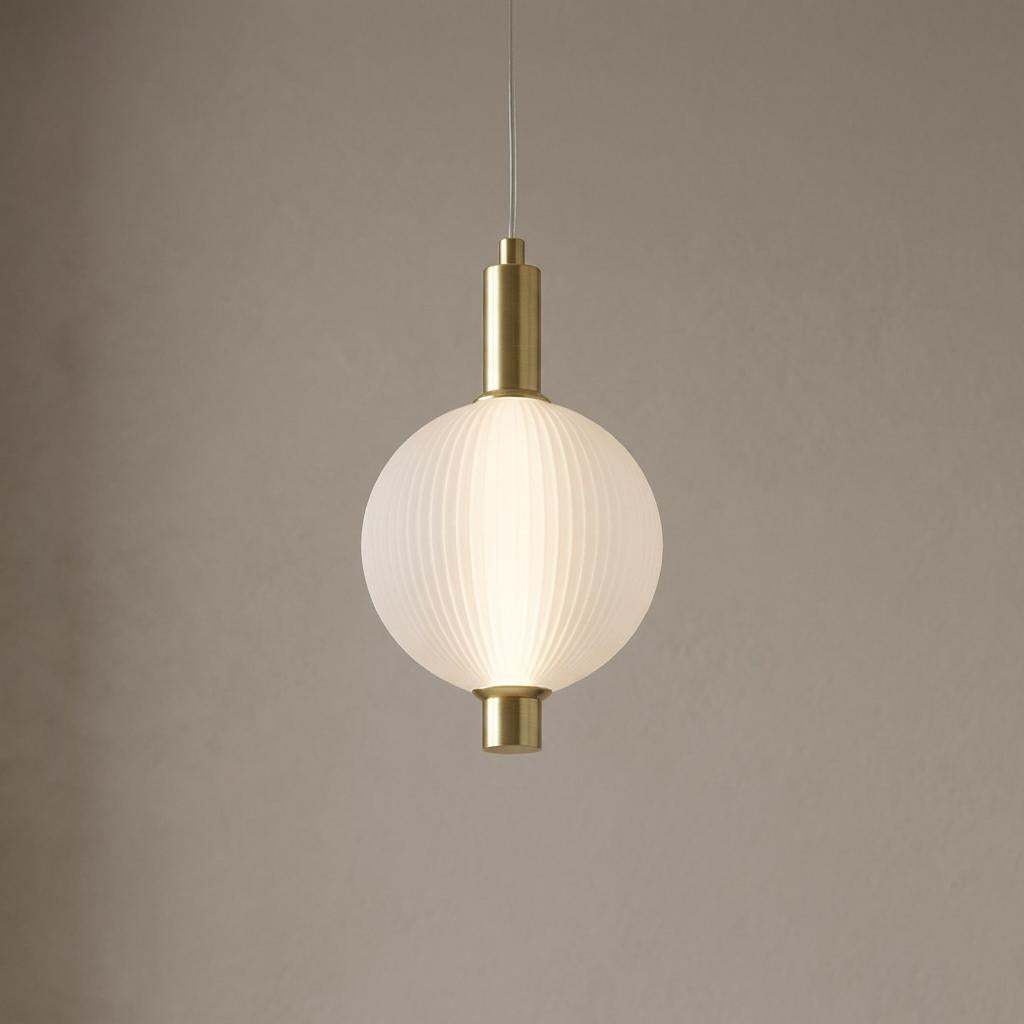 A glowing, ribbed white glass pendant light with satin brass fixtures hanging against a textured beige wall.