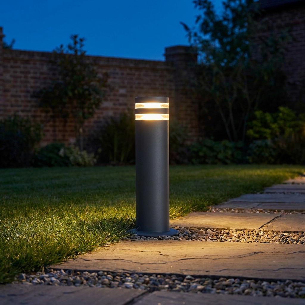 A grey cylindrical bollard light illuminates a stone garden pathway with two glowing bands at night.