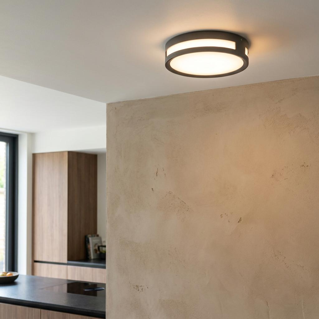An illuminated Lutec Rola grey flush ceiling light mounted on an indoor ceiling above a textured plaster wall.