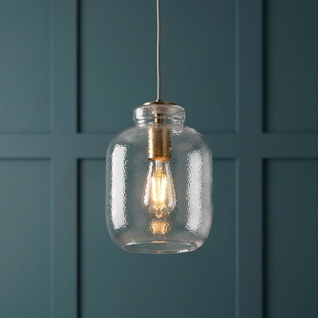 Lyra brass and clear textured glass pendant light illuminated in front of a teal paneled wall.